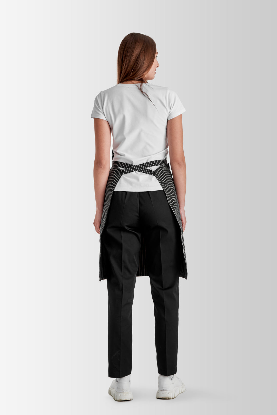 Back view of a woman wearing a gray pinstripe bib apron with waist ties