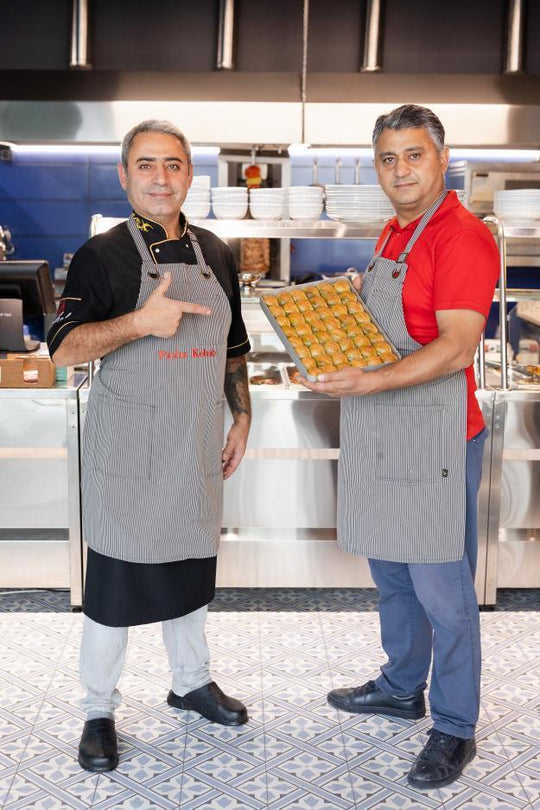 Two restaurant staff wearing gray pinstripe bib aprons while presenting a tray of pastries