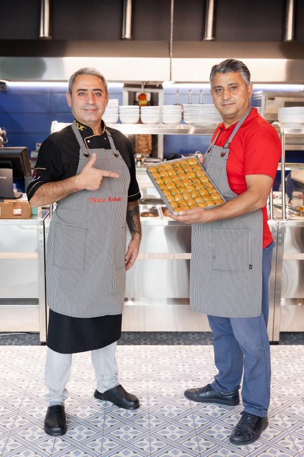 Two restaurant staff wearing gray pinstripe bib aprons while presenting a tray of pastries