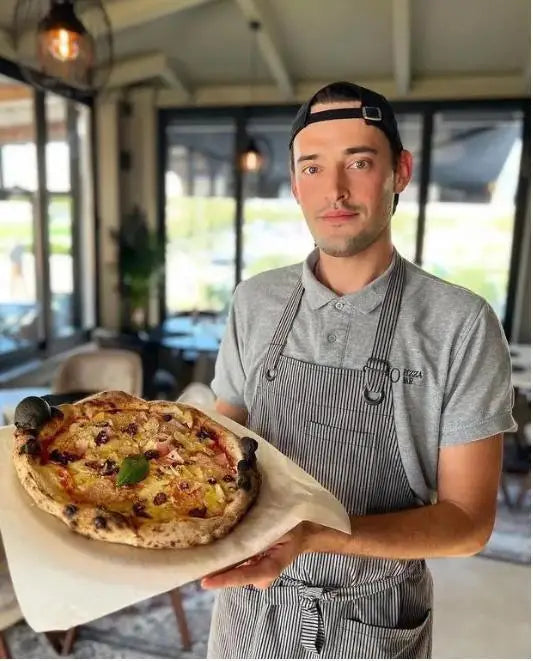 Pizza chef wearing a gray pinstripe bib apron while holding a fresh pizza