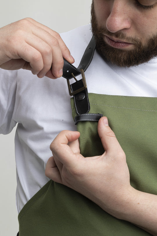 Close-up of green bib apron with adjustable black neck strap and metal buckle