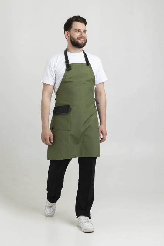 Man wearing a green bib apron with black adjustable straps and flap pocket