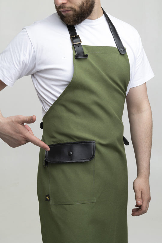 Man wearing a green bib apron with black adjustable straps and flap pocket