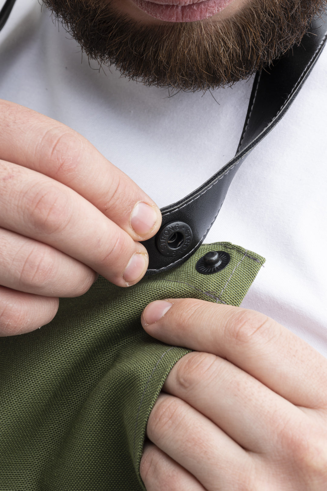 Close-up of green bib apron with detachable black strap and snap fastener