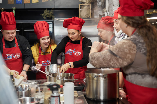 Cooking class participants wearing red bib aprons with logos and matching chef hats