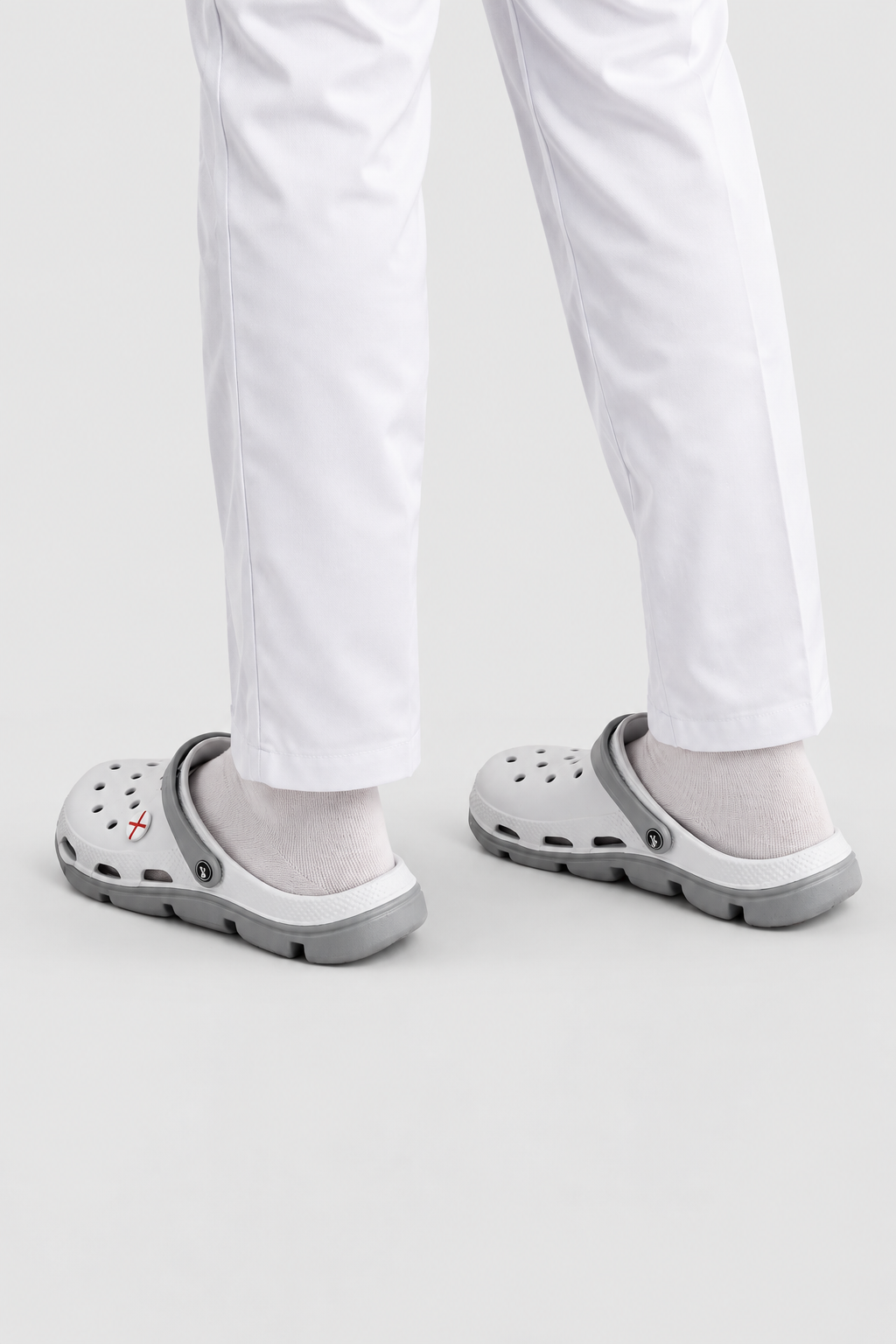 White pants with white socks and gray clogs shown from the feet up against a light gray studio background.