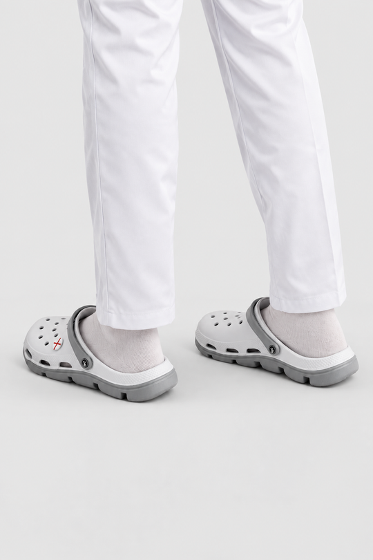 White pants with white socks and gray clogs shown from the feet up against a light gray studio background.