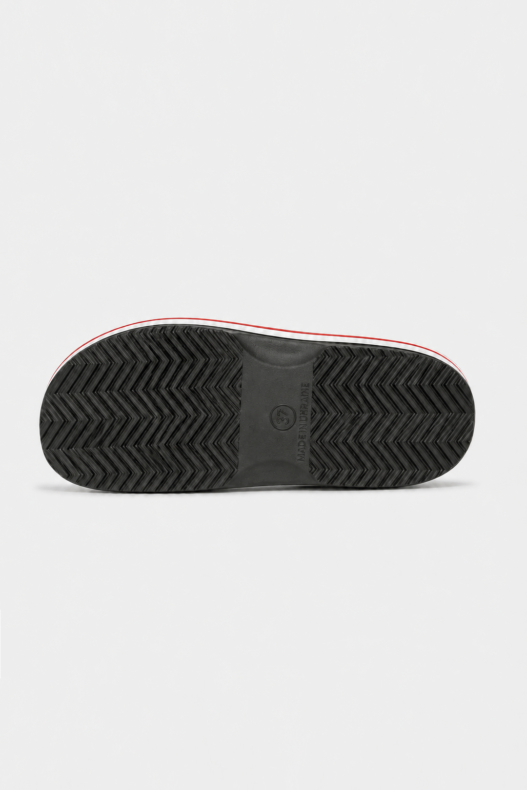 The black textured rubber outsole of a sneaker, showing a herringbone tread pattern and a thin red and white stripe along the edge, photographed from directly below on a light gray background.