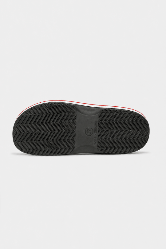 The black textured rubber outsole of a sneaker, showing a herringbone tread pattern and a thin red and white stripe along the edge, photographed from directly below on a light gray background.