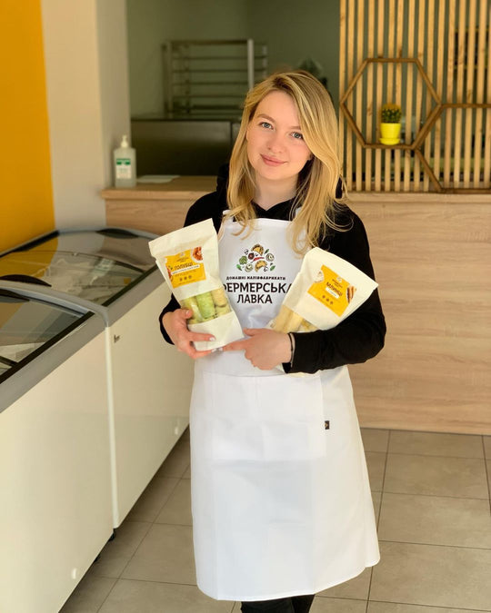 Woman wearing a white bib apron with logo while holding packaged products in a retail shop