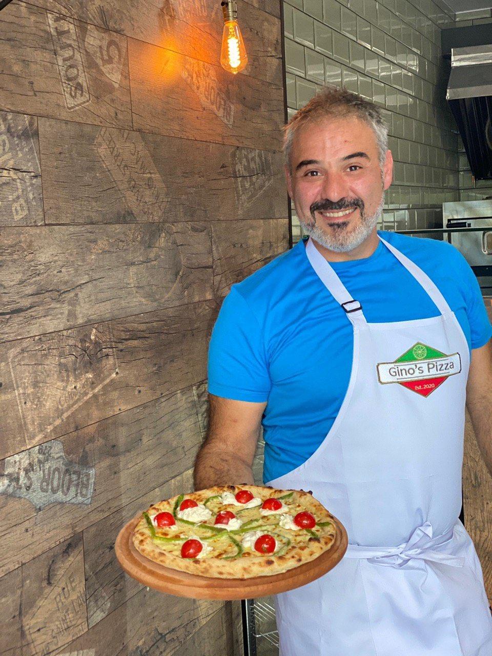 Pizza chef wearing a white bib apron with logo while holding a fresh pizza